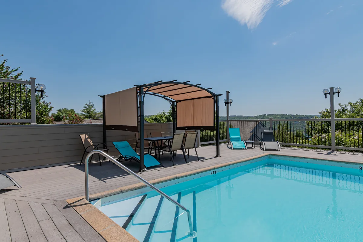 A welcoming outdoor pool area with a canopy structure and lounge chairs, suggesting a tranquil setting for swimming, sunbathing, or socializing. The pool is surrounded by greenery, reinforcing the natural, relaxing environment.
