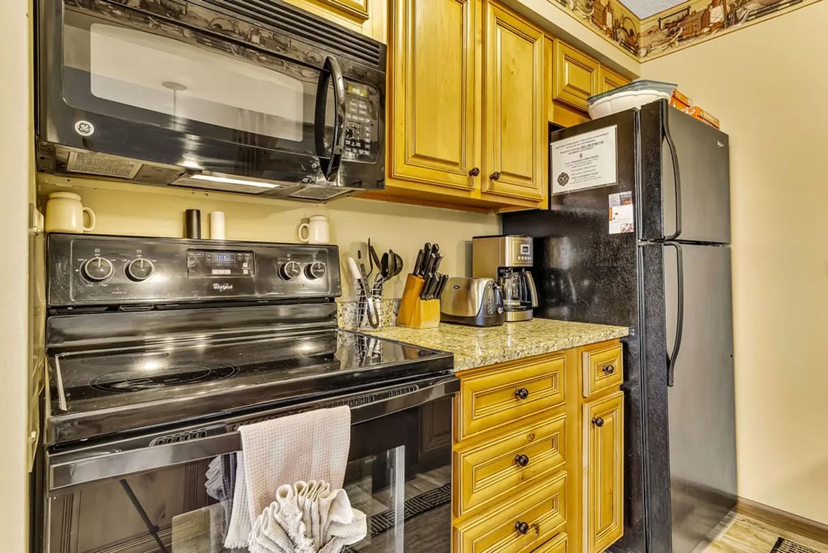A warm, inviting kitchen featuring gleaming granite countertops, wooden cabinetry, and modern stainless steel appliances. Kitchen utensils are neatly arranged, and the space feels designed for both cooking and entertaining.