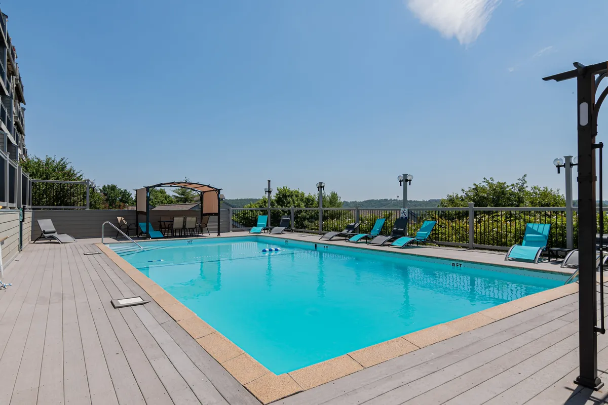 A bright, inviting outdoor pool area with sparkling water, plenty of lounge chairs, and a canopy-covered seating area. The setting is perfect for relaxing, socializing, or enjoying the sun during the pool's open season.