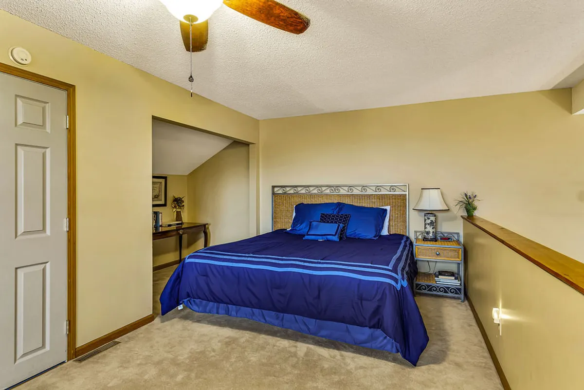 A tranquil bedroom with a neatly made bed, nightstand, decorative plant, and tasteful wall art. The soft lighting and cozy arrangement create a restful environment for sleep or relaxation.