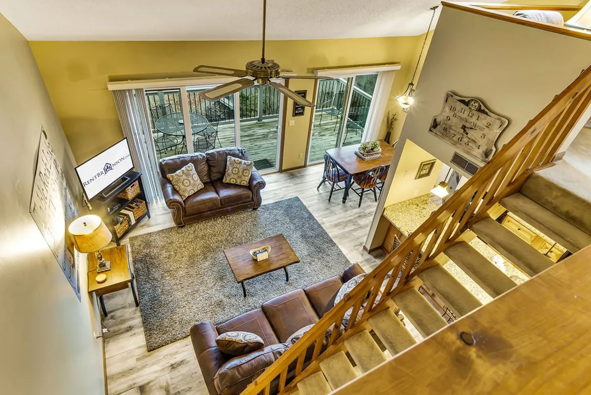A bright, open-concept living and dining area featuring a plush brown leather sofa, a welcoming dining table for group meals, and expansive windows showcasing stunning lake views. The space radiates warmth with cozy furnishings and natural light flooding in, perfect for gathering and relaxing with loved ones.