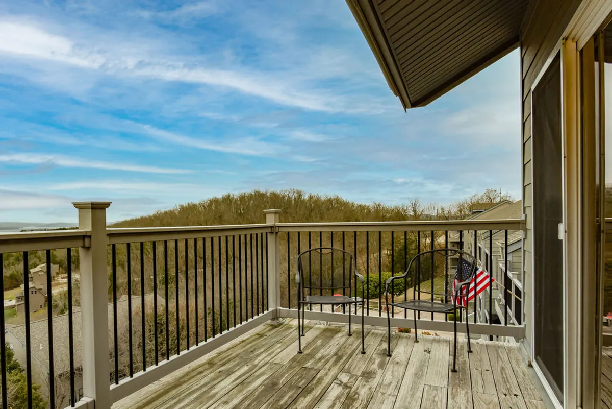 A peaceful balcony scene featuring two chairs positioned behind a railing, an American flag, and distant tree-lined hills. The space offers a private vantage point for enjoying sunrise coffee or sunset over the lake, blending comfort with natural beauty.