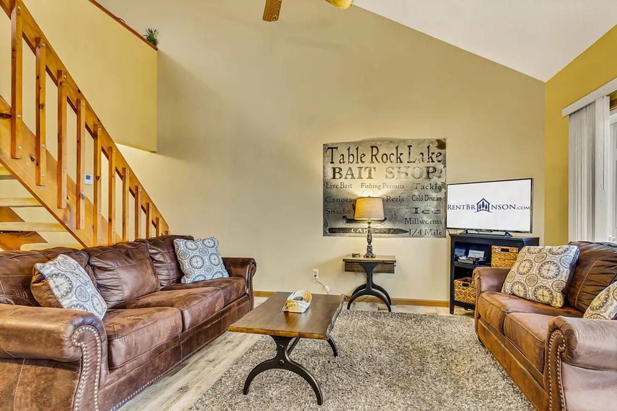 A comfortable living area with a leather sofa, decorative pillows, coffee table, wall art, and a TV stand, set in a warm, inviting space ideal for relaxation or socializing.